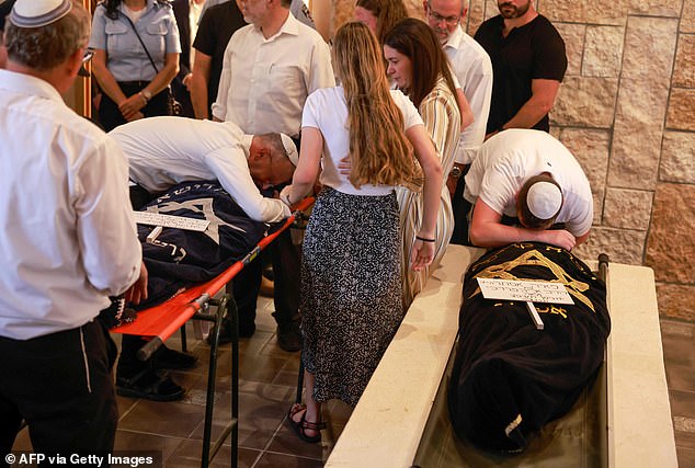 يتكئ الأقارب على الجثث المغطاة بالأخوات حزينًا في جنازتهما في عيد الفصح