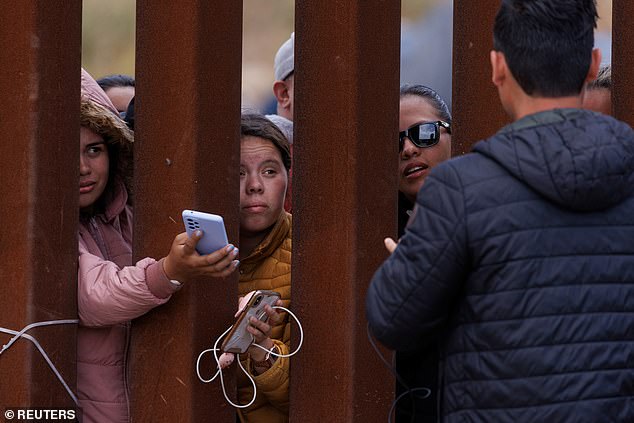 يتواصل المهاجرون من السياج الحدودي في محاولة لشحن هواتفهم وهم عالقون بين السياجين الحدوديين الأساسي والثانوي