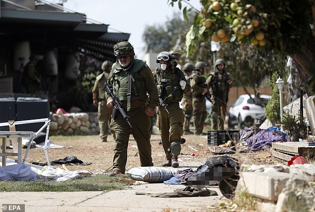 جنود إسرائيليون يسيرون بجانب جثث أحد نشطاء حماس الذين قُتلوا في كيبوتز كفار عزة يوم الثلاثاء