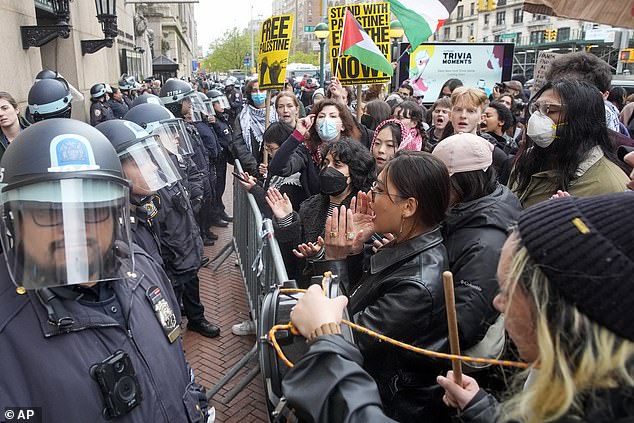 ضباط شرطة مدينة نيويورك يرتدون معدات مكافحة الشغب يقفون للحراسة بينما يردد المتظاهرون شعارات خارج حرم جامعة كولومبيا، الخميس 18 أبريل 2024