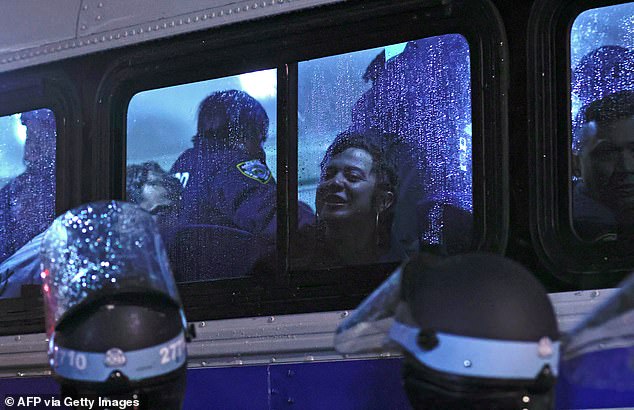 يُرى أحد المتظاهرين من خلال نافذة حافلة شرطة نيويورك الممطرة بينما يقوم الضباط بتحميلهم بعد طردهم من مبنى المدرسة