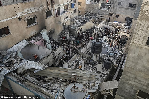 فلسطينيون يتفقدون مبنى عائلة العطار المدمر جراء العدوان الإسرائيلي بجوار عيادة الأمم المتحدة في مخيم يبنا برفح