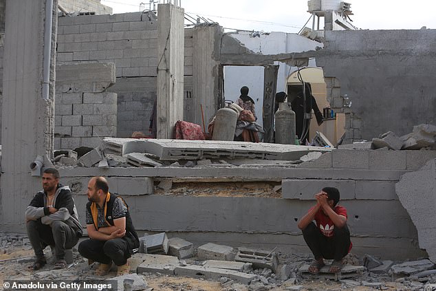 أشخاص يجلسون أمام مبنى مهدم بينما يبحث الفلسطينيون عن أشياء صالحة للاستخدام بين أنقاض المبنى المدمر