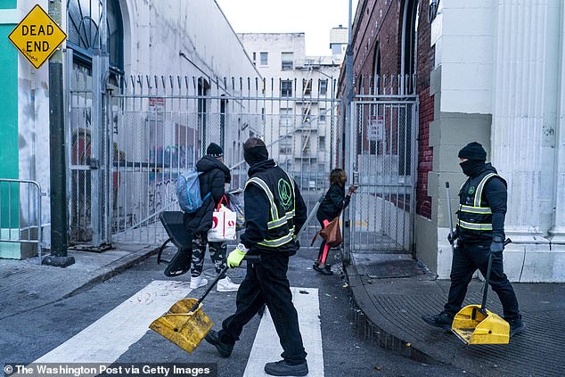 في الصباح الباكر، يلتقط رجل وامرأة بلا مأوى متعلقاتهما بسرعة بينما تبدأ أطقم Urban Alchemy التنظيف اليومي للشوارع في حي Tenderloin في سان فرانسيسكو.