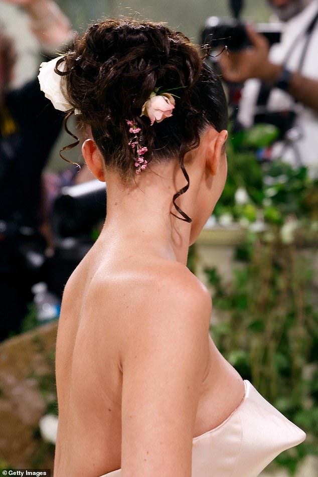 تم سحب الشعر البني الداكن لمؤسس شركة Kylie Cosmetics إلى الخلف في تسريحة مرفوعة ضيقة وتم تثبيت حلقاتها النطاطة بأزهار نضرة.