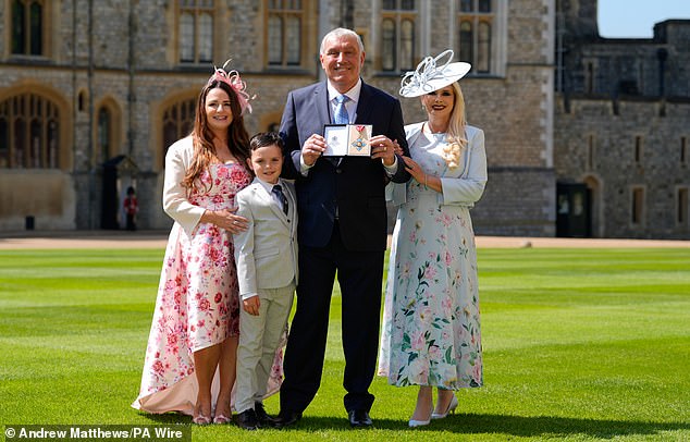 بيتر شيلتون يقف لالتقاط صورة مع زوجته ستيف شيلتون (يمين) وعائلتهم بعد حصوله على وسام الإمبراطورية البريطانية